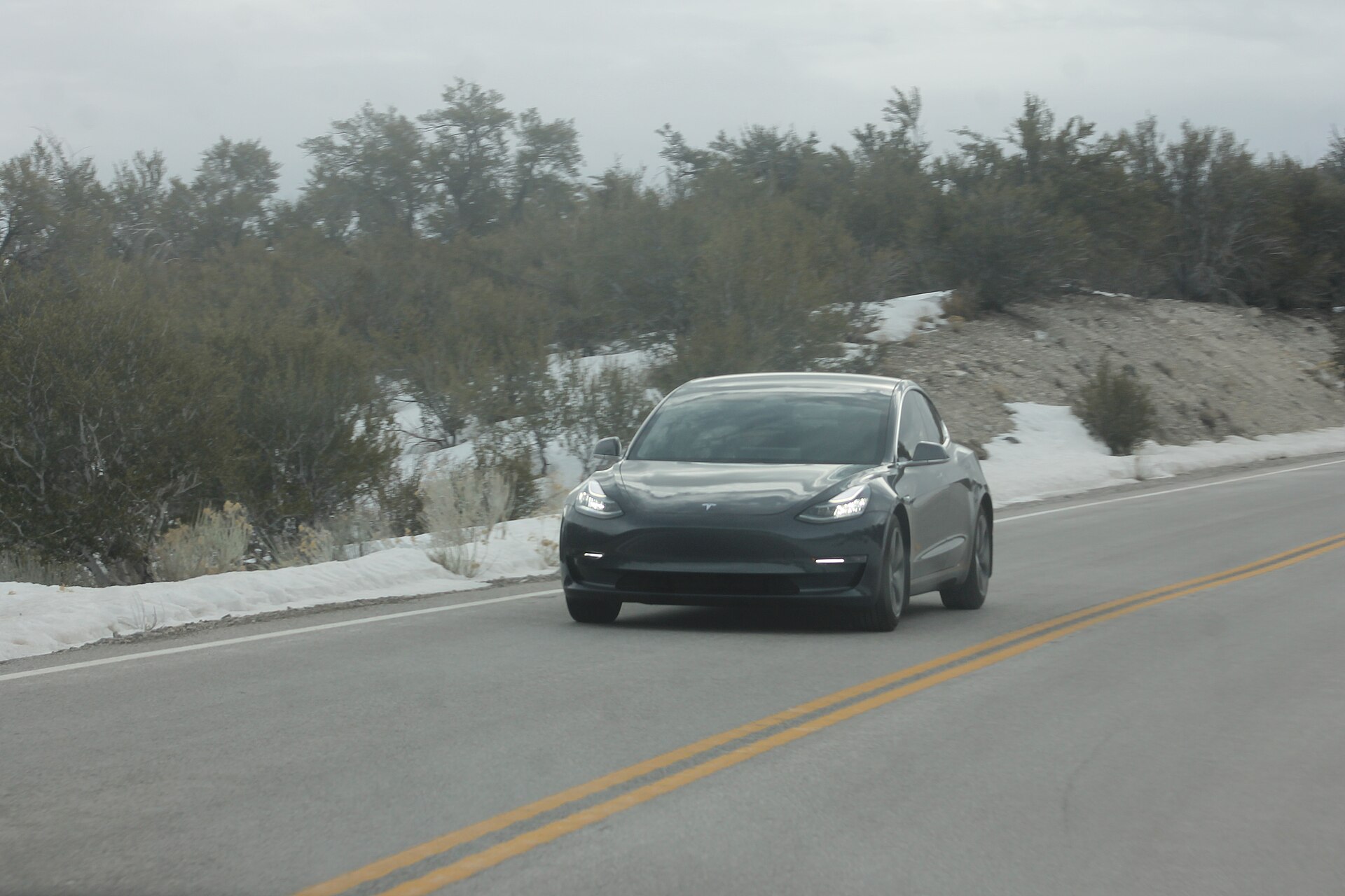 Grey Tesla Model 3 driving on a snow-lined mountain road