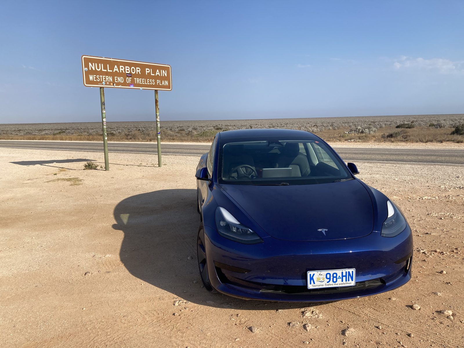 Tesla Model 3 parked on a long, open highway during a long-distance drive