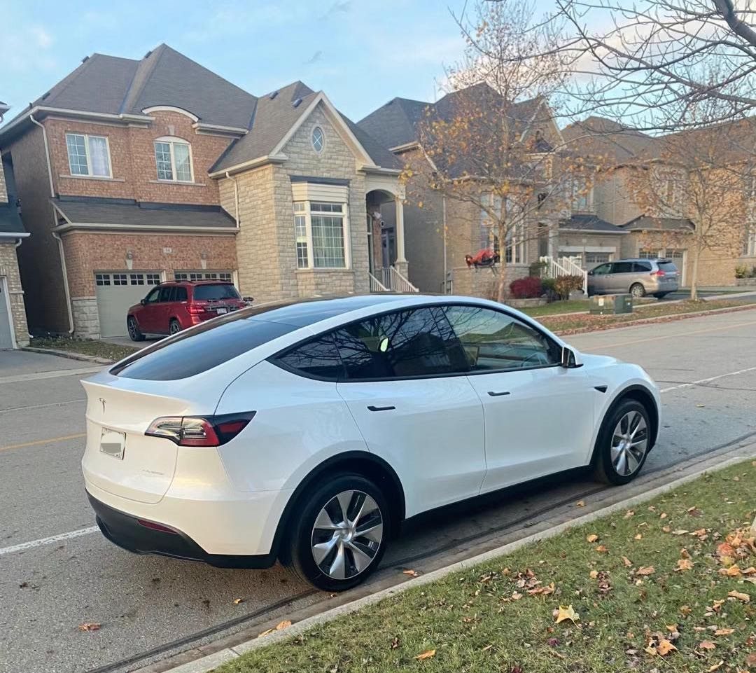 Rear three-quarter view of a white Tesla Model Y Long Range on an Ontario street, autumn leaves on the ground
