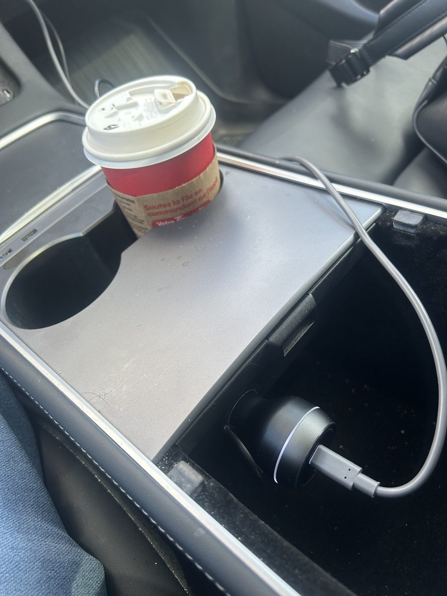 Tesla Model Y centre console open, with the car charger inside and the power cable routed out over the edge of the storage bin