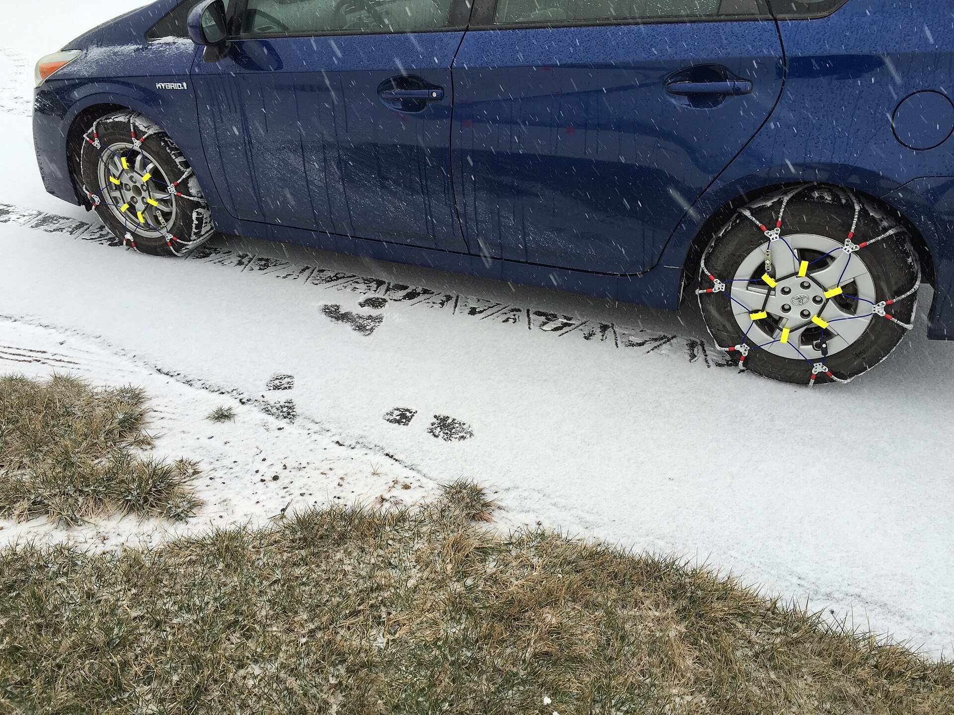 Cable snow chains fitted to a car tire on a snowy road during a winter storm