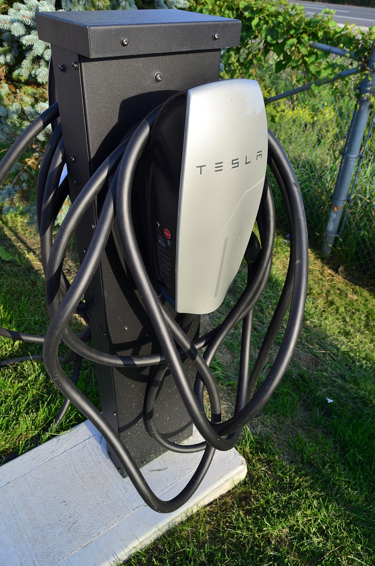 Tesla destination charger mounted on a black pedestal with its cable coiled