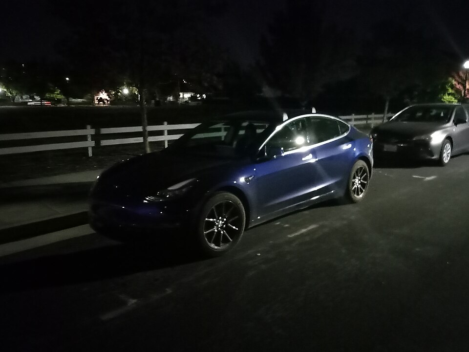 Blue Tesla Model 3 parked at night in a parking lot