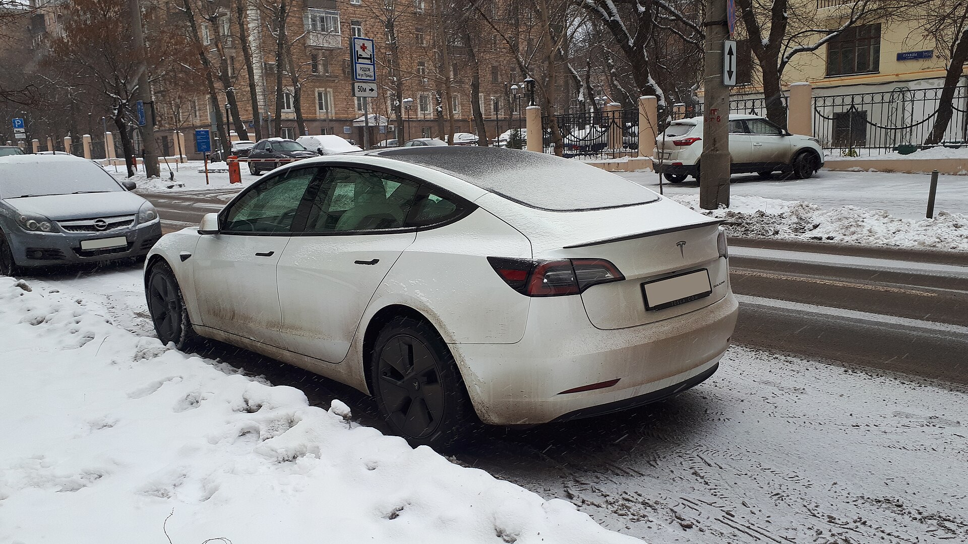 White Tesla Model 3 parked on a snowy street, with snow on the glass roof and salt on the doors